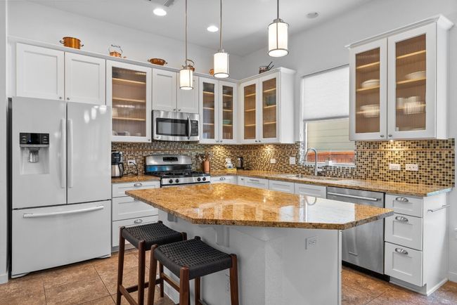 Kitchen featuring white cabinetry, a kitchen island, decorative backsplash, stainless steel appliances, and hanging light fixtures | Image 10