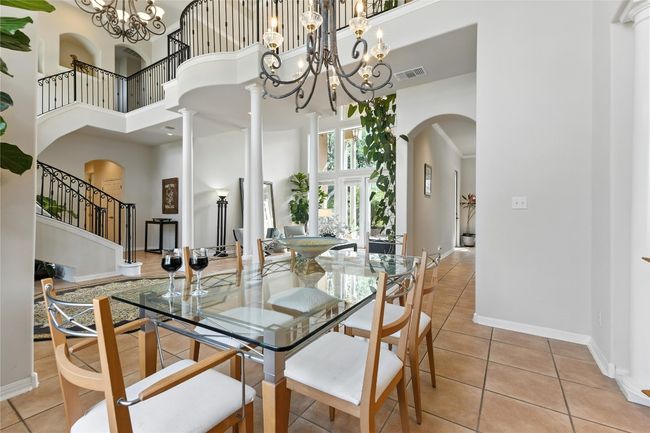 Dining area featuring a high ceiling, light tile patterned flooring, arched walkways, a chandelier, and stairs | Image 11