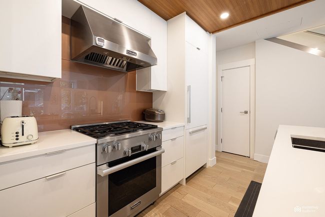 Kitchen featuring light countertops, wall chimney range hood, high end stainless steel range oven, and white cabinetry | Image 9
