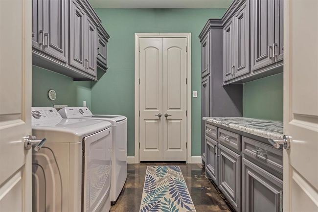 The spacious laundry room is designed for convenience, featuring ample storage cabinets, a generous folding counter, and double doors that open to an additional large storage closet. Washer and dryer are included with the home, making this space fully equipped and move-in ready. | Image 14