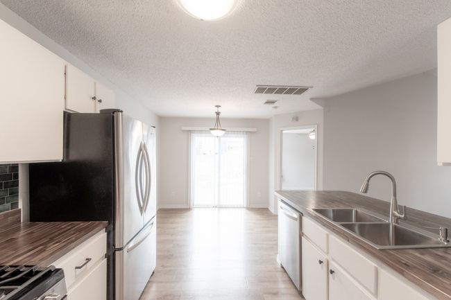Kitchen featuring appliances with stainless steel finishes, a textured ceiling, light wood finished floors, white cabinetry, and hanging light fixtures | Image 13