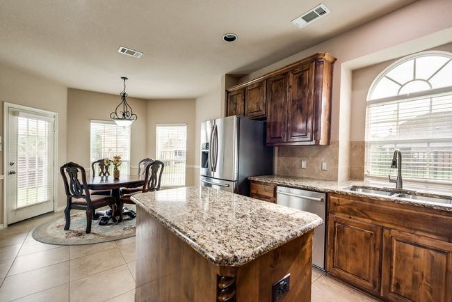 Kitchen featuring appliances with stainless steel finishes, a sink, a kitchen island, light stone countertops, and tasteful backsplash | Image 13