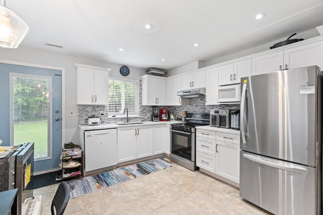 Kitchen with appliances with stainless steel finishes, under cabinet range hood, a sink, tasteful backsplash, and recessed lighting | Image 23
