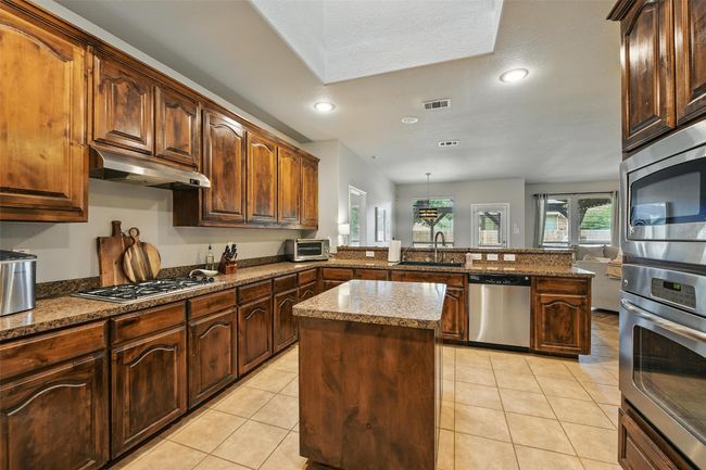 Kitchen featuring stainless steel appliances, a peninsula, under cabinet range hood, a center island, and light tile patterned floors | Image 18