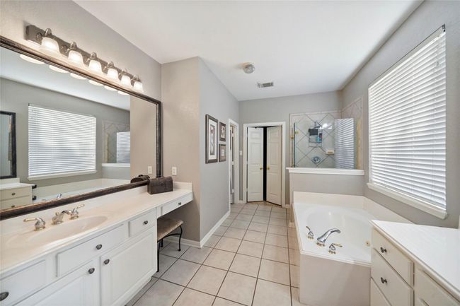 This spacious bathroom features a large vanity with dual sinks, ample storage, a relaxing soaking tub, and a separate shower. Natural light floods in through multiple windows, enhancing the bright and airy atmosphere. | Image 21