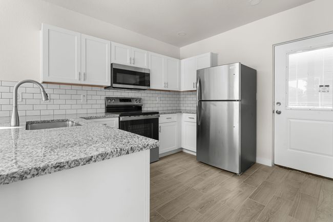 Kitchen with stainless steel appliances, white cabinets, light stone countertops, and tasteful backsplash | Image 6