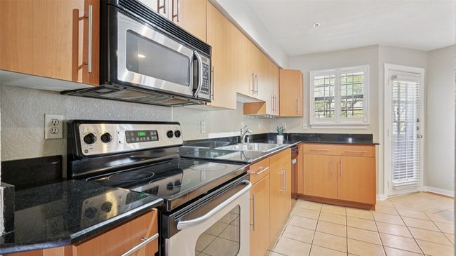 Kitchen with stainless steel appliances, a sink, light tile patterned floors, and dark stone countertops | Image 12
