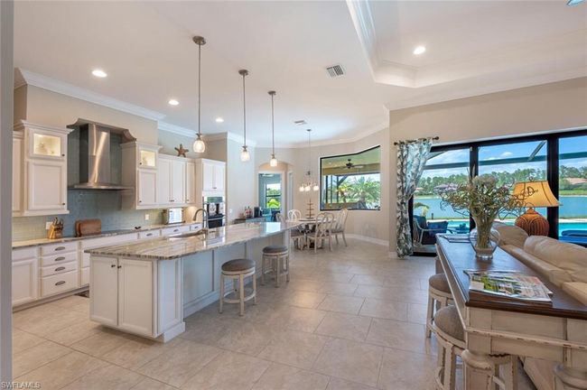 Kitchen featuring wall chimney range hood, a sink, light stone counters, backsplash, and an island with sink | Image 16