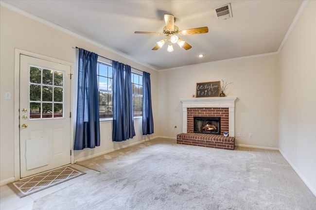 Unfurnished living room featuring a ceiling fan, crown molding, carpet flooring, a brick fireplace, and baseboards | Image 6