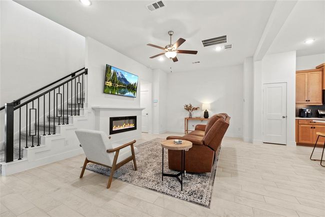 The family room boasts an electric fireplace, ceiling fan and high ceiling. | Image 7