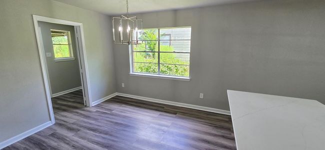 Bright dining area with modern chandelier, large window, and open layout leading to a sleek kitchen with white cabinetry and a spacious countertop. | Image 8