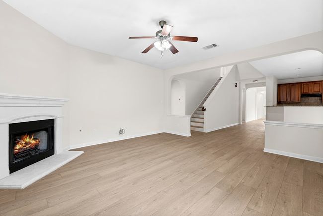 Unfurnished living room with a warm lit fireplace, ceiling fan, stairway, light wood-style flooring, and arched walkways | Image 9
