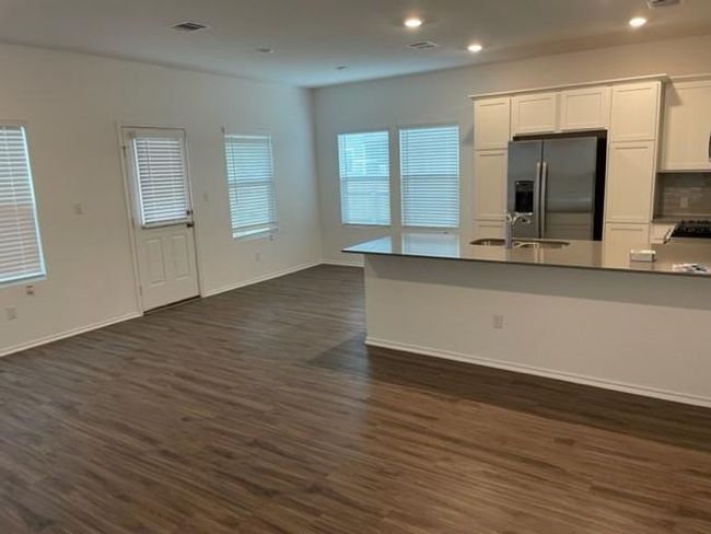 Kitchen with stainless steel fridge with ice dispenser, a sink, white cabinetry, dark wood-type flooring, and open floor plan | Image 8