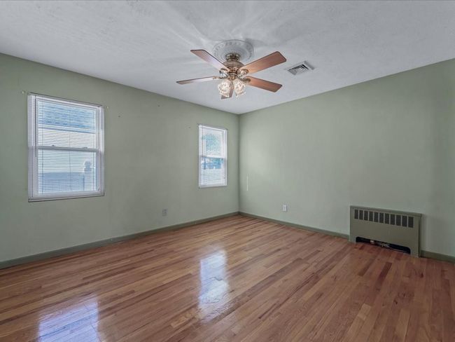 Spare room with radiator, wood finished floors, and a ceiling fan | Image 12