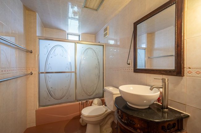 Bathroom featuring tile walls, shower / bath combination with glass door, vanity, and toilet | Image 21