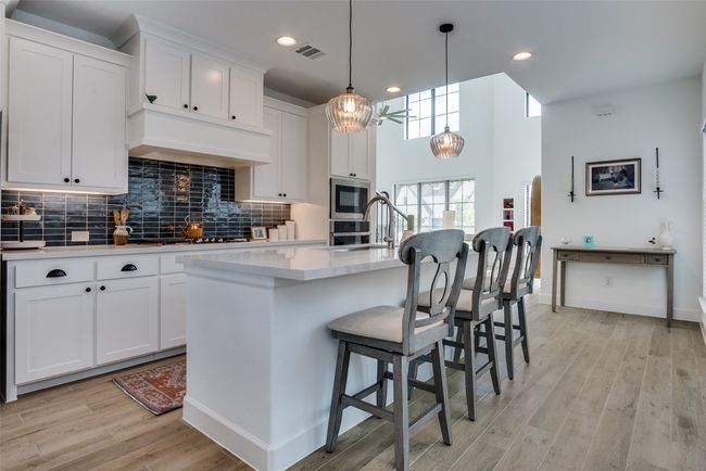Kitchen with black microwave, light countertops, decorative backsplash, light wood finished floors, and white cabinets | Image 15