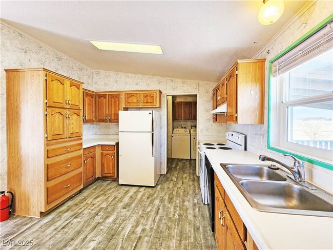 Kitchen with a sink, light wood-style floors, washer and clothes dryer, vaulted ceiling, and white appliances | Image 10