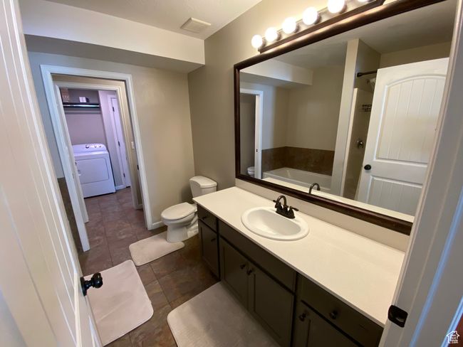 Bathroom with washer / clothes dryer, a bath, toilet, vanity, and tile patterned floors | Image 13