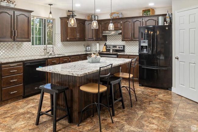 Kitchen with decorative backsplash, black appliances, a center island, and dark brown cabinetry | Image 6