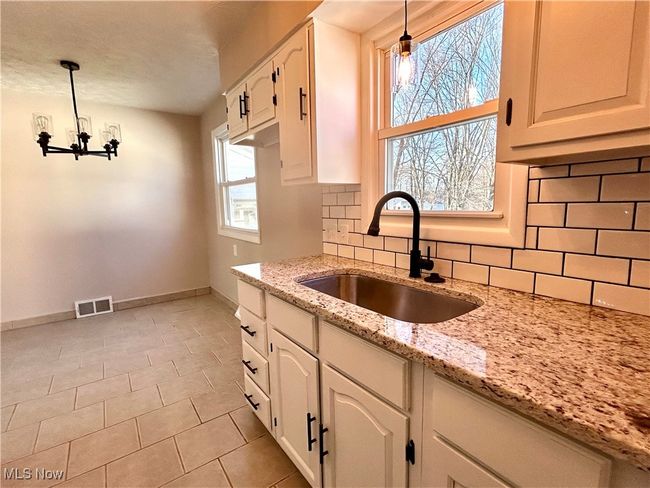 Kitchen featuring a chandelier, white cabinets, a sink, new granite and backsplash. | Image 4