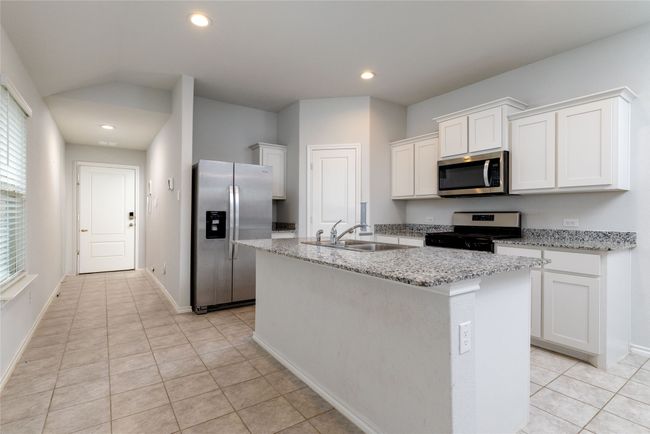 Kitchen featuring stainless steel appliances, a sink, white cabinetry, light tile patterned floors, and an island with sink | Image 5