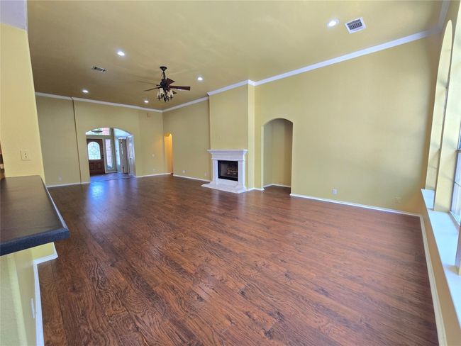 Unfurnished living room with arched walkways, a ceiling fan, ornamental molding, wood finished floors, and a fireplace with raised hearth | Image 11