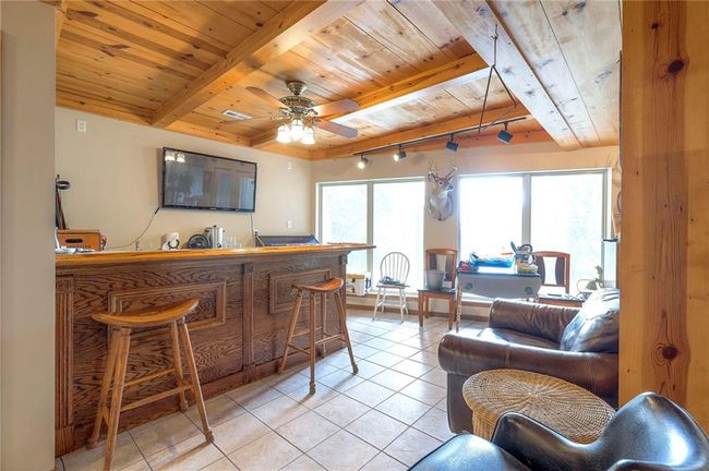 Indoor bar with a wood ceiling with exposed beams, light tile patterned flooring, rail lighting, and ceiling fan | Image 32