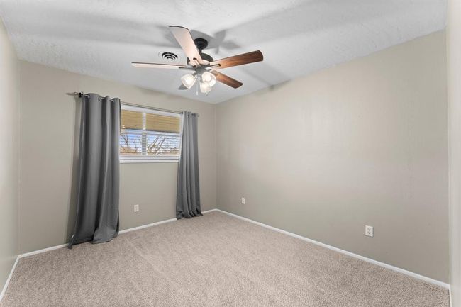 This bedroom features neutral walls and carpet, a ceiling fan with lights, and a window to provide ample natural light. | Image 20