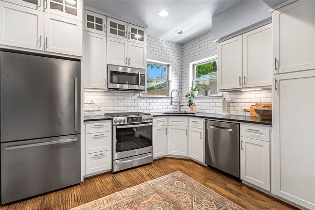 Kitchen featuring appliances with stainless steel finishes, a sink, dark countertops, glass insert cabinets, and dark wood-style flooring | Image 8