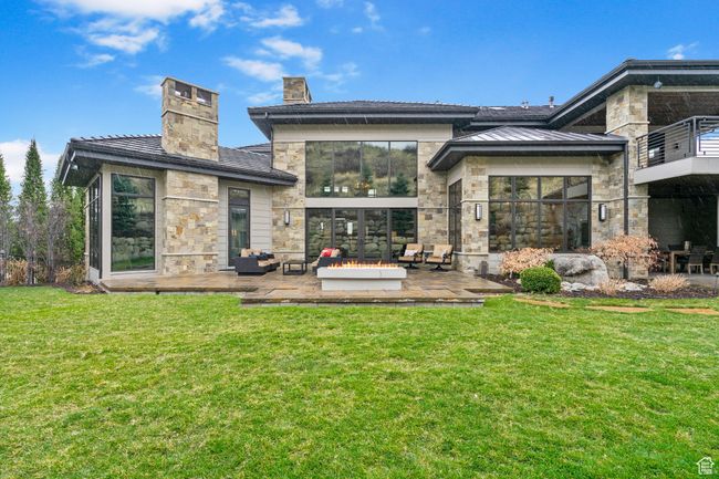 Back of house featuring a patio area, stone siding, a lawn, a chimney, and an outdoor living space | Image 112