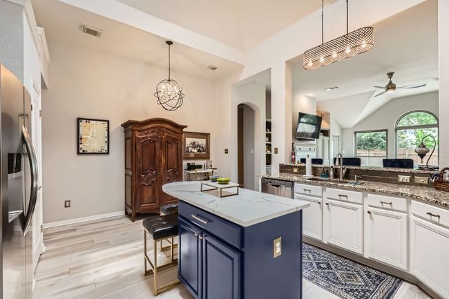Kitchen featuring arched walkways, a chandelier, stainless steel appliances, white cabinetry, and quartz center island | Image 9