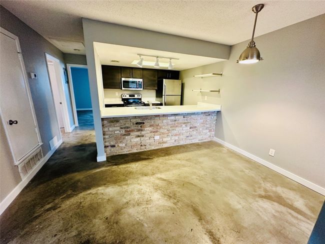 Kitchen with concrete flooring, appliances with stainless steel finishes, a textured ceiling, hanging light fixtures, and a peninsula | Image 8