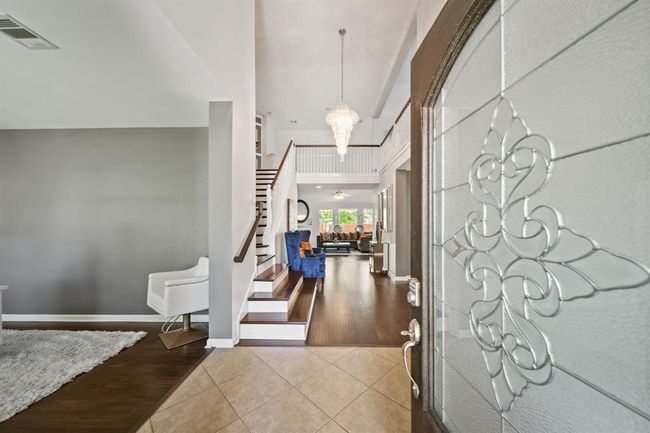 Step through the elegant glass-paneled front door into a soaring two-story foyer with a dramatic chandelier, tile entry, and rich wood flooring that flows seamlessly throughout the main living areas. | Image 6