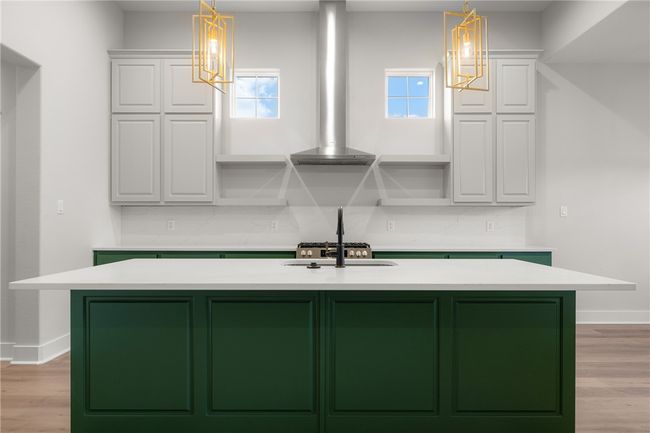 Kitchen featuring wall chimney range hood, an island with sink, hanging light fixtures, white cabinetry, and light hardwood / wood-style flooring | Image 12