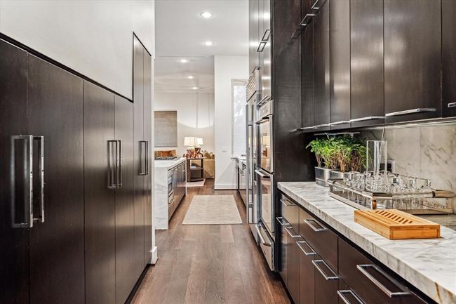 Providing a multitude of cabinet and counter space is the BUTLER'S PANTRY with its custom stained wood cabinetry, built-in cabinet wall, designer fixtures, marble slab counter/backsplash, under cabinet lighting, wide plank flooring and recessed lighting. | Image 9
