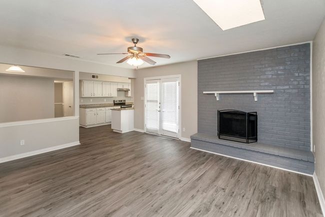 Unfurnished living room with ceiling fan, wood finished floors, a fireplace, and a skylight | Image 4