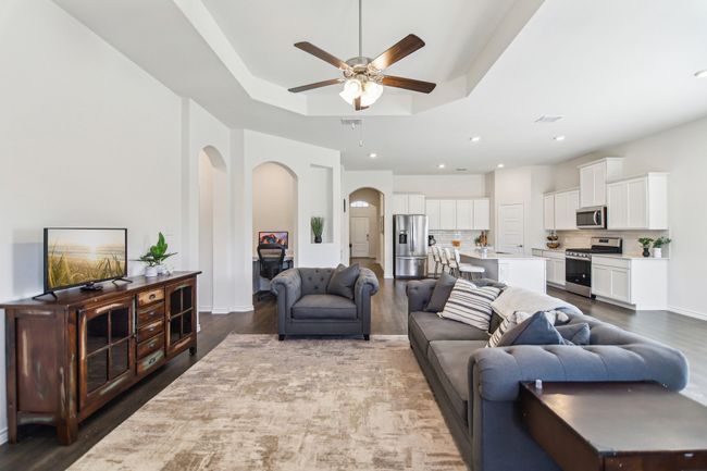 Living room featuring arched walkways, a tray ceiling, a ceiling fan, and wood finished floors | Image 7