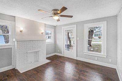 Unfurnished living room featuring a textured ceiling, a fireplace, ceiling fan, and dark wood-type flooring- Previous photos | Image 3