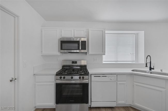 Kitchen featuring stainless steel appliances, white cabinets, light countertops, and wood finished floors | Image 11