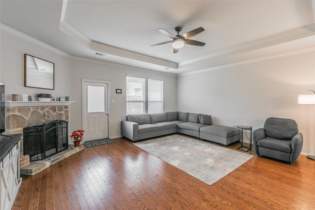 Living room with a stone fireplace, ceiling fan, hardwood / wood-style floors, a tray ceiling, and ornamental molding | Image 22
