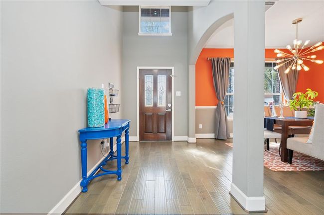 Bright and inviting entryway with high ceilings and hardwood floors. Features a striking blue console table and leads into a dining area with orange accent walls and modern lighting. Natural light fills the space through large windows. | Image 11