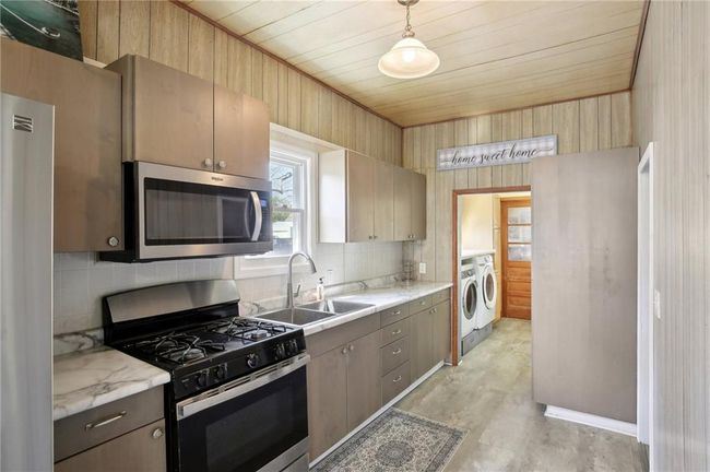 Kitchen featuring stainless steel appliances, backsplash, wooden ceiling, a sink, and washer and dryer | Image 9