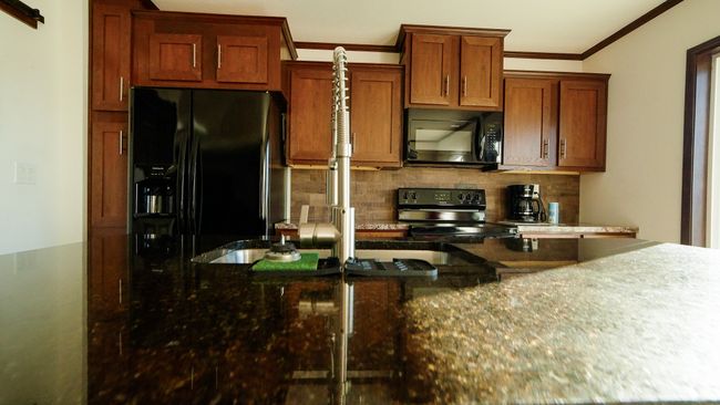 Kitchen featuring dark stone countertops, brown cabinetry, decorative backsplash, black appliances, and crown molding | Image 32