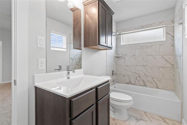 Secondary bath features tile flooring, bath/shower combo with tile surround, stained wood cabinets, beautiful light countertops, mirror, dark, sleek fixtures and modern finishes. | Image 16