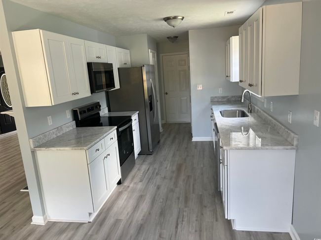 Kitchen featuring appliances with stainless steel finishes, light wood-style floors, white cabinetry, and light stone countertops | Image 6
