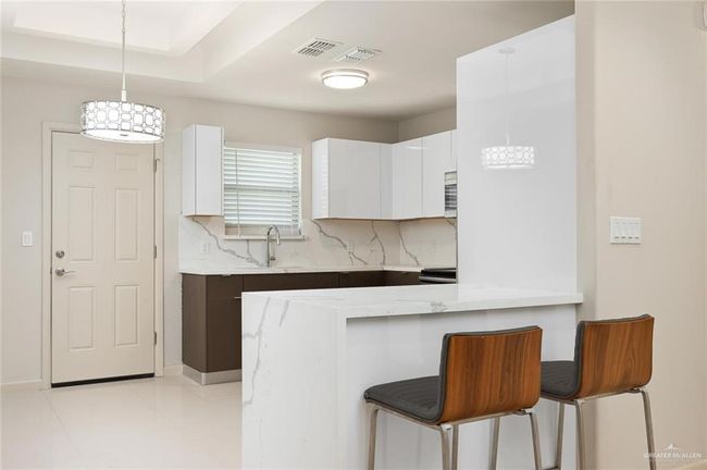Kitchen with backsplash, white cabinetry, a breakfast bar area, a peninsula, and pendant lighting | Image 6