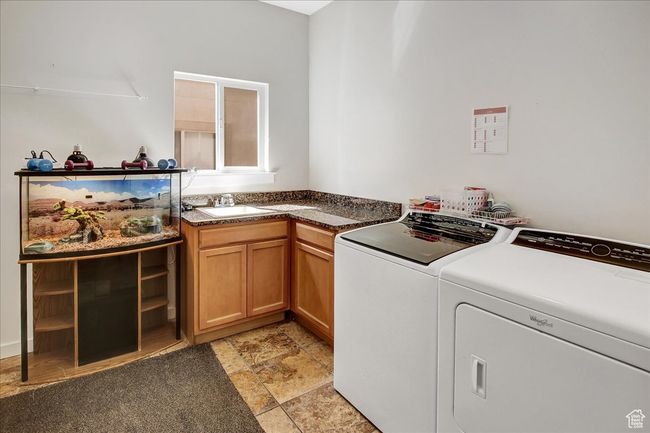 Clothes washing area featuring washing machine and dryer, cabinet space, a sink, and stone finish flooring | Image 16