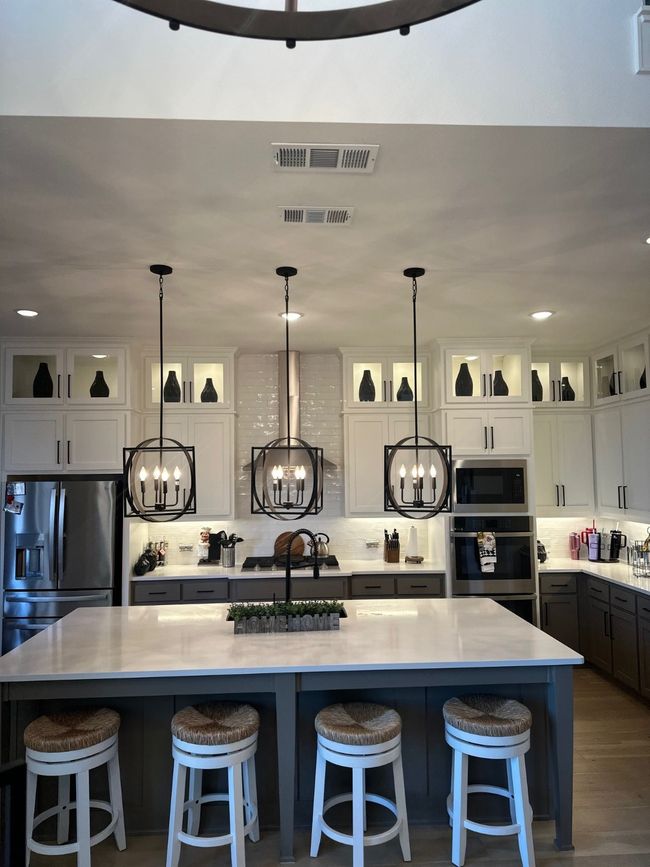 Kitchen featuring wall oven, light countertops, hanging light fixtures, fridge, and a center island with sink | Image 13
