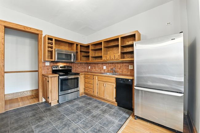 Spacious kitchen featuring stainless steel range, microwave, and refrigerator, complemented by custom wood cabinetry and tiled backsplash. | Image 13