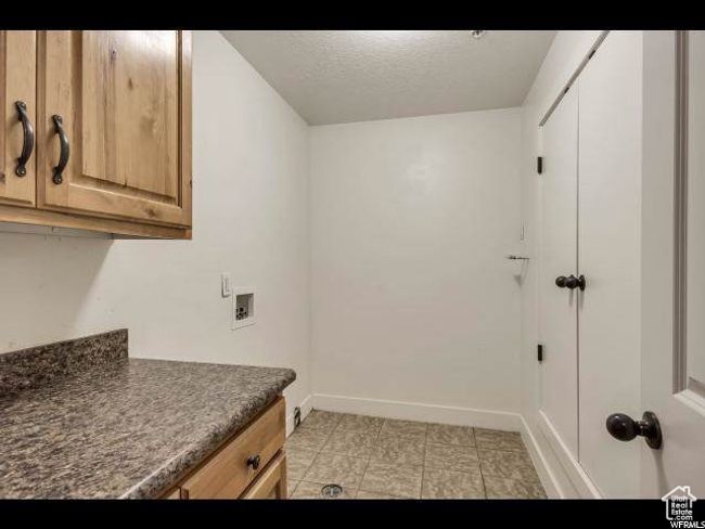 Laundry room with cabinet space, washer hookup, baseboards, a textured ceiling, and light tile patterned floors | Image 12